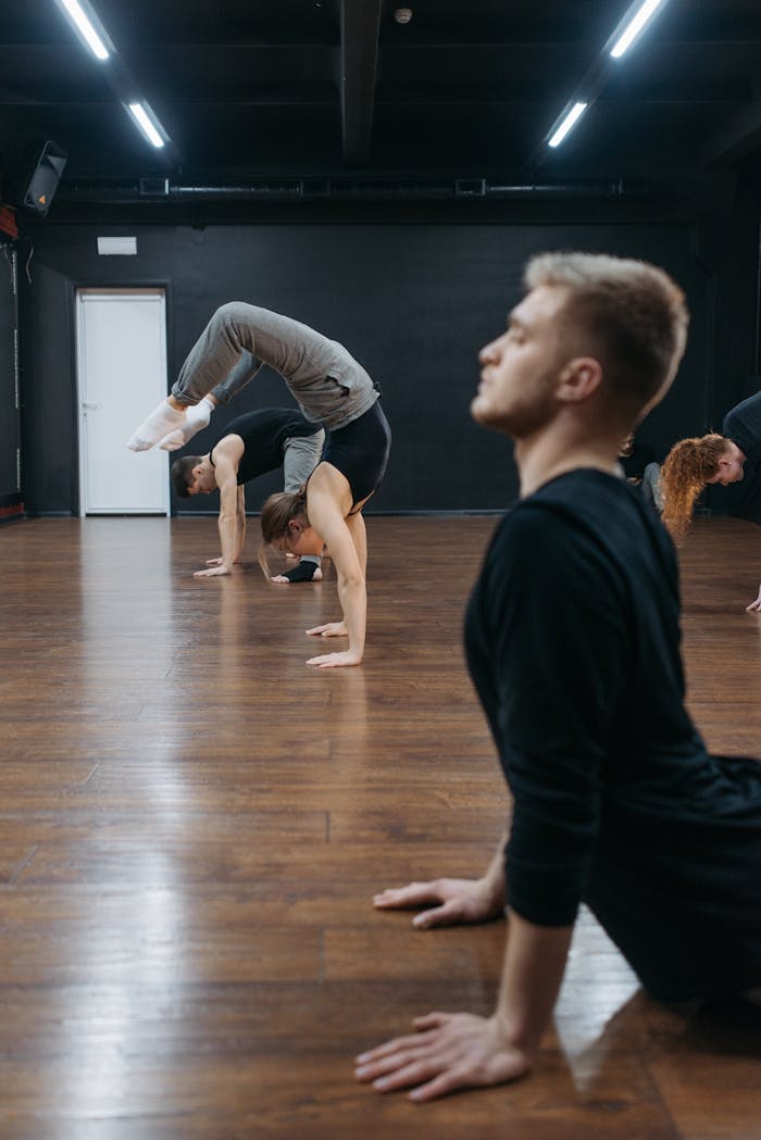 A group of adults stretching and practicing flexibility in a dance studio.